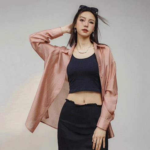 Woman wearing a pink shirt over a black top and skirt on a plain background